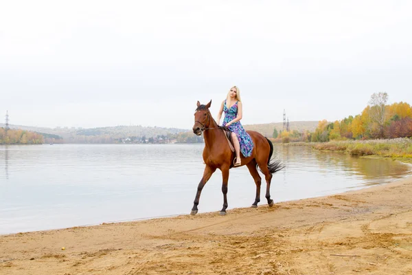 Ein Mädchen im Abendkleid springt auf einem Pferd am Ufer eines Teiches — Stockfoto
