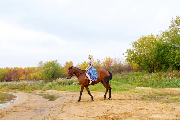 Bir göl kıyısında bir atlı bir akşam elbiseli bir kız atlar