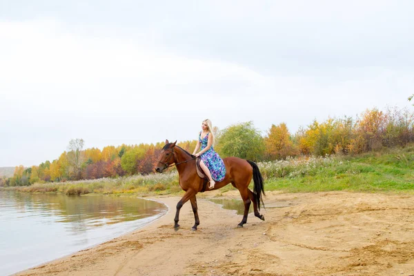 Bir göl kıyısında bir atlı bir akşam elbiseli bir kız atlar