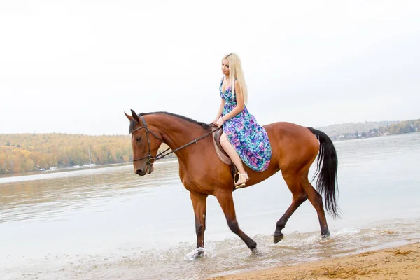 Bir göl kıyısında bir atlı bir akşam elbiseli bir kız atlar