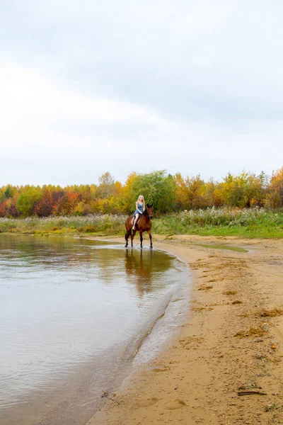 Bir göl kıyısında bir atlı bir akşam elbiseli bir kız atlar