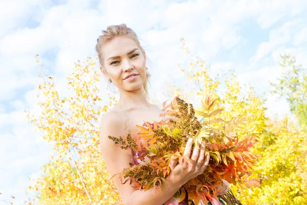 Mädchen mit einem Strauß gelber Herbstblätter im Wald — Stockfoto