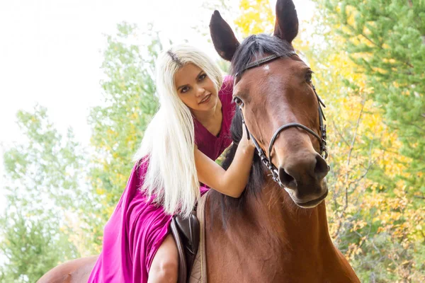 金发女郎骑着一匹马在一个秋天的树林 — 图库照片