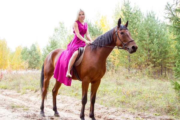 Blonde riding a horse in an autumn forest — Stock Photo, Image