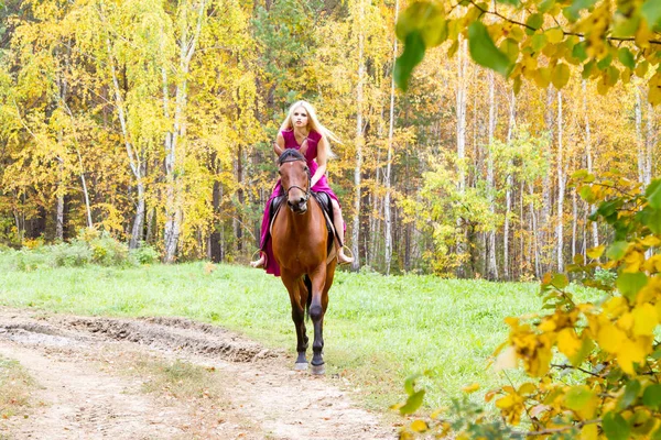 Blondine reitet in einem herbstlichen Wald — Stockfoto