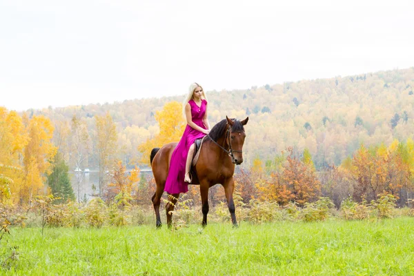 Blondin i en aftonklänning rider en häst — Stockfoto