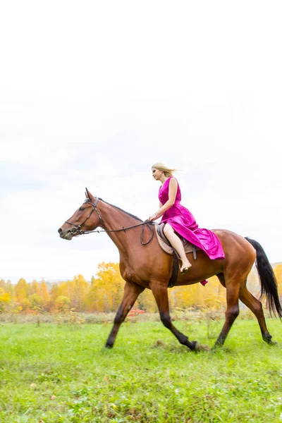Blondýnka ve večerních šatech jezdí na koni — Stock fotografie