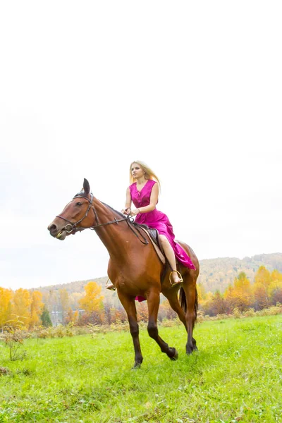 Loira em um vestido de noite monta um cavalo — Fotografia de Stock