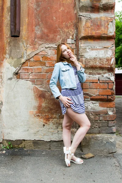 Meisje in een kort rokje is permanent door de bakstenen muur van een oud huis — Stockfoto