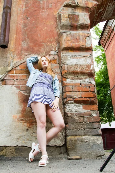 Mädchen im kurzen Rock steht an der Ziegelwand eines alten Hauses — Stockfoto