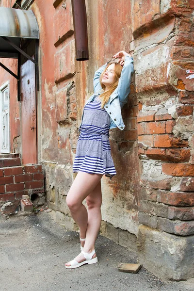 Chica en una falda corta está de pie junto a la pared de ladrillo de una casa vieja —  Fotos de Stock