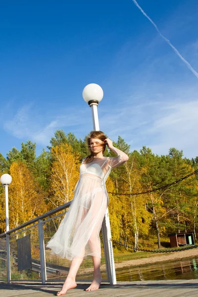 Girl in a transparent dress is walking along the picturesque shore of the pond — Stock Photo, Image