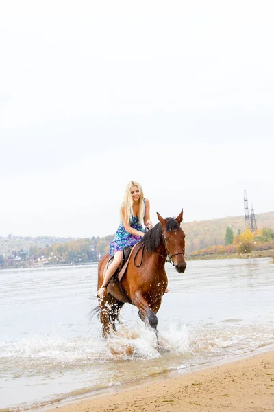 Ung blondin rider en häst hoppar längs bukten — Stockfoto