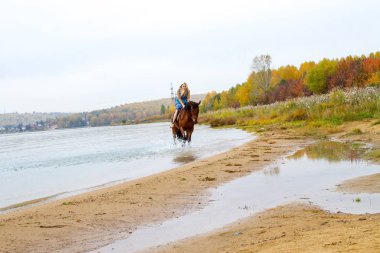Genç sarışın bir binicilik Körfezi kıyı atlar