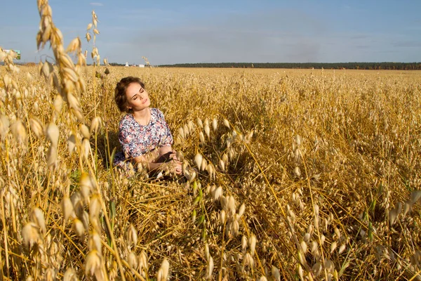 Junge Bäuerin sitzt auf einem Feld zwischen reifen Ähren — Stockfoto