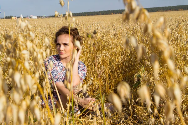 Junge Bäuerin sitzt auf einem Feld zwischen reifen Ähren — Stockfoto