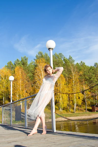 Jovem em um vestido branco transparente na costa de uma lagoa pitoresca — Fotografia de Stock