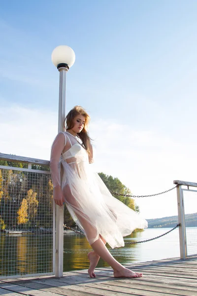 Young girl in a transparent white dress on the shore of a picturesque pond — Stock Photo, Image