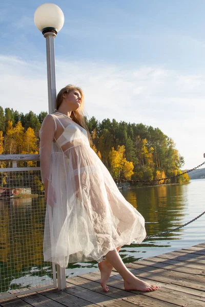 Young girl in a transparent white dress on the shore of a picturesque pond — Stock Photo, Image