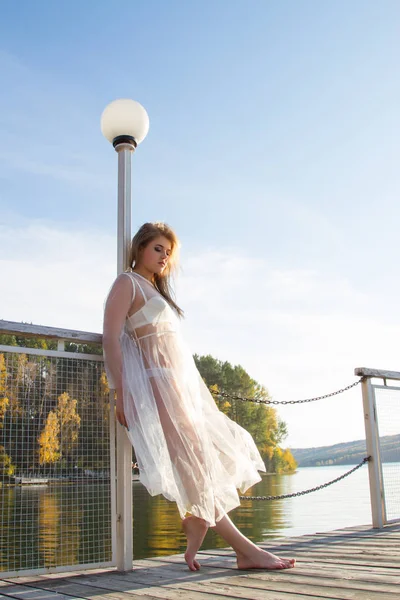 Junges Mädchen in einem transparenten weißen Kleid am Ufer eines malerischen Teiches — Stockfoto