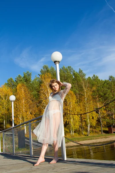 Giovane ragazza in un abito bianco trasparente sulla riva di un pittoresco stagno — Foto Stock