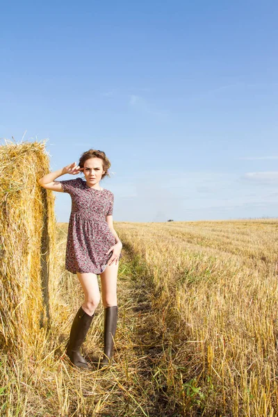 Fille est debout dans un champ près d'une balle de paille — Photo