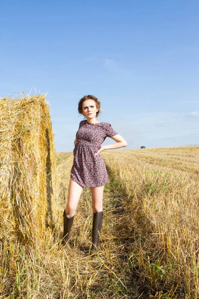 Fille est debout dans un champ près d'une balle de paille — Photo