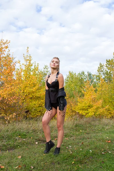 Sexy junges Mädchen in Lederjacke und Munition zwischen den Herbstblättern — Stockfoto