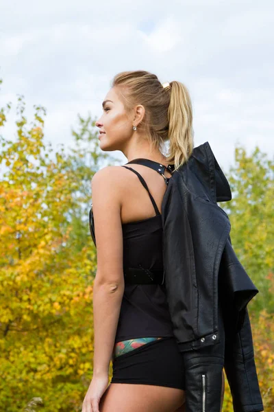 Sexy junges Mädchen in Lederjacke und Munition zwischen den Herbstblättern — Stockfoto