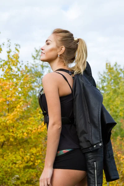 Sexy junges Mädchen in Lederjacke und Munition zwischen den Herbstblättern — Stockfoto