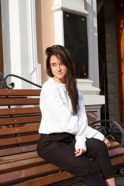 건물 배경에 벤치에 앉아 하얀 스웨터에 어린 소녀 — 스톡 사진