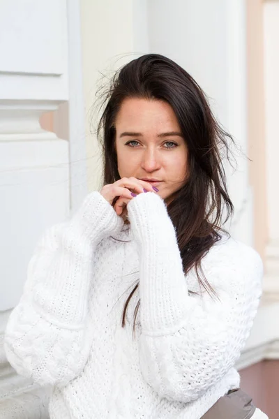 Young girl in white sweater sits on building background — Stock Photo, Image