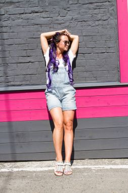 güneş gözlüklü kız bir tuğla duvara yakın duruyor