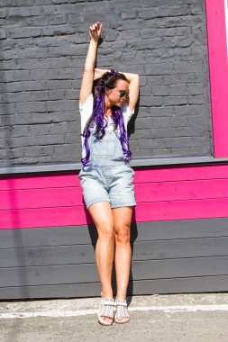 güneş gözlüklü kız bir tuğla duvara yakın duruyor