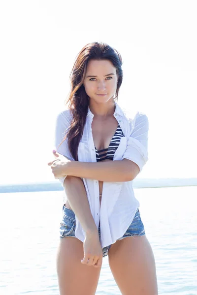 Girl on the beach in a white shirt and short denim shorts — Stock Photo, Image