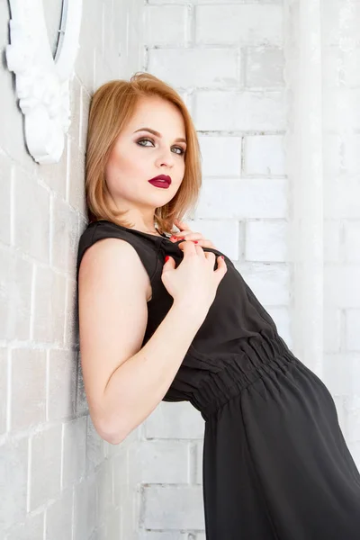 Szőke egy rövid fekete ruhás ellen egy téglafal háttér — Stock Fotó