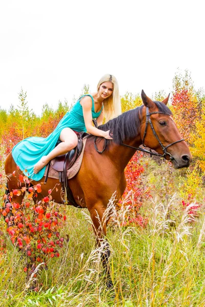 Loira montando um cavalo caminha pela floresta de outono — Fotografia de Stock
