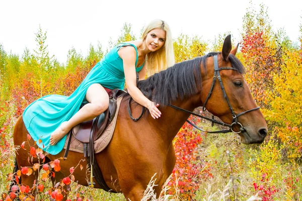Blonde riding a horse walks through the autumn forest — Stock Photo, Image