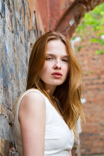 Red-haired girl against the shabby wall of a dilapidated house — Stock Photo, Image