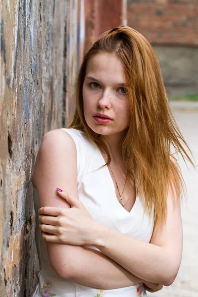 Red-haired girl against the shabby wall of a dilapidated house — Stock Photo, Image