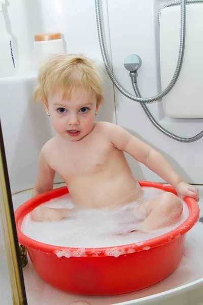 小さな子供が降り注ぐ赤い洗面器 — ストック写真