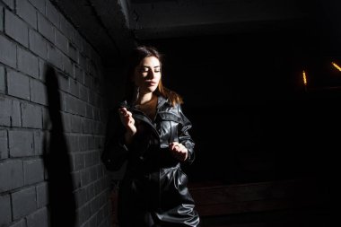 Karanlık bir odada siyah deri tulumlu güzel bir genç kız.