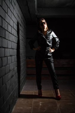 Karanlık bir odada siyah deri tulumlu güzel bir genç kız.