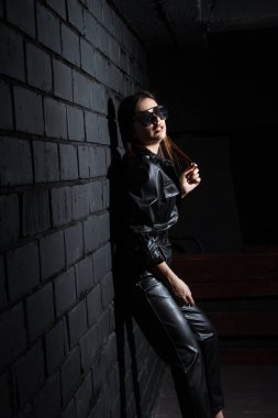 Karanlık bir odada siyah deri tulumlu güzel bir genç kız.