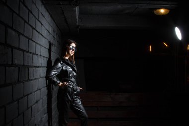 Karanlık bir odada siyah deri tulumlu güzel bir genç kız.