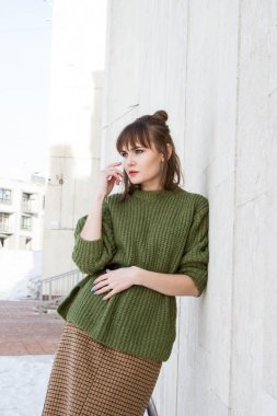 Yeşil kazaklı genç kız mermer duvara yaslanmış duruyor.