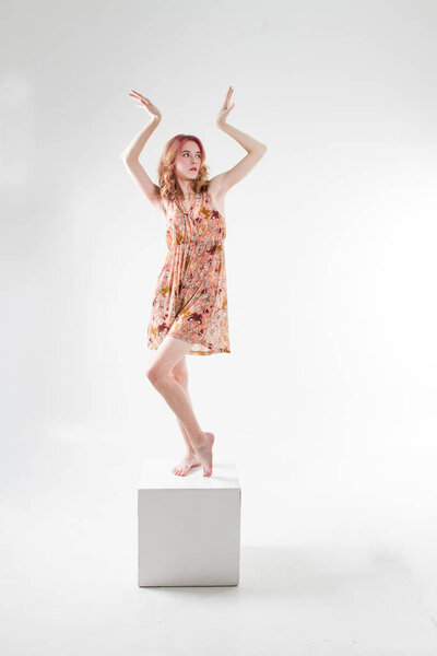 Young beautiful girl stands on barefoot cube and in a dress
