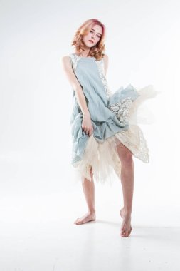 Genç ve güzel bir kız çıplak ayaklı ve beyaz bir arka planda poz veren bir elbise giyiyor. Stüdyo resmi.