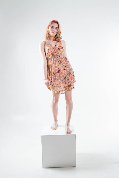 Young beautiful girl stands on barefoot cube and in a dress