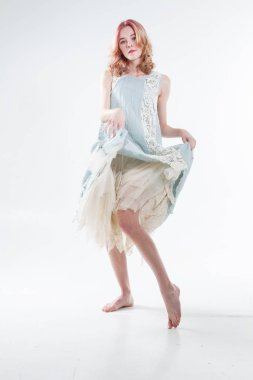 Barefoot blonde in a long dress. Studio portrait on a white background.